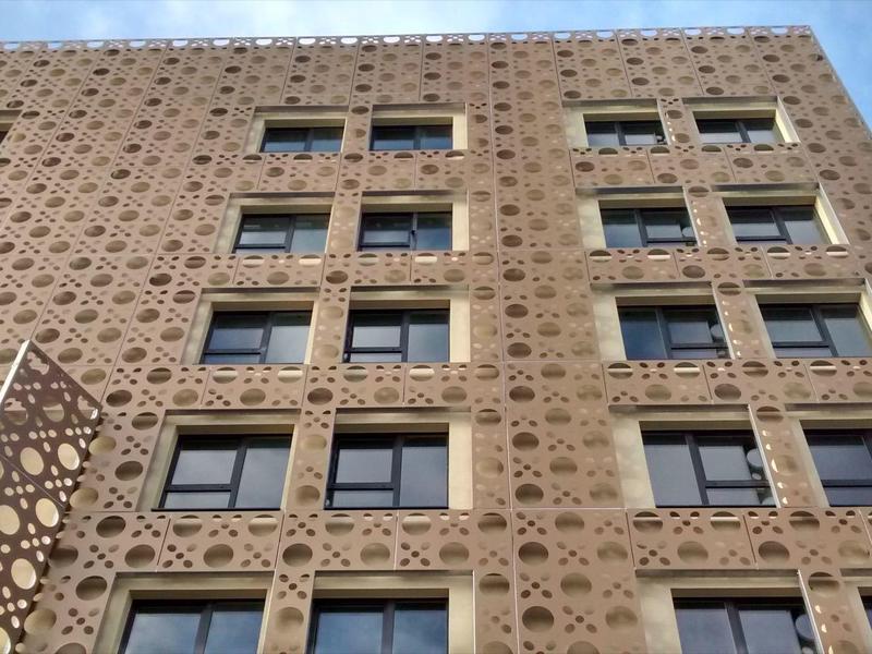 Fassade eines hohen Gebäudes mit geometrischem Lochmuster und mehreren Rechteckfenstern.