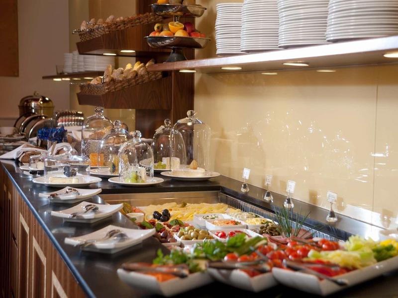 Buffet mit Tellerstapel, frischem Gemüse, Salaten und Besteck auf dunkler Arbeitsplatte.