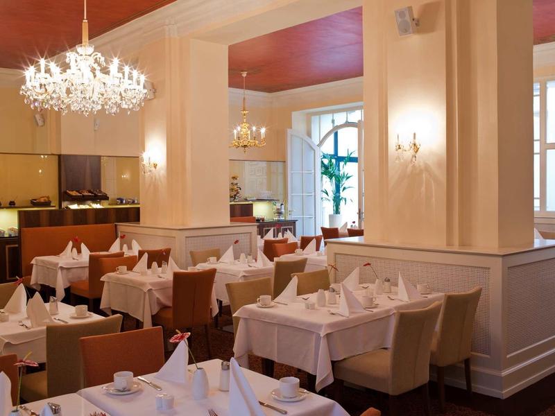 Elegantes Restaurant mit weiß gedeckten Tischen, beigen Stühlen und Kronleuchtern an der Decke.