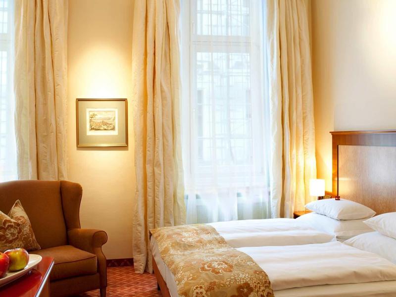 Ein helles Hotelzimmer mit zwei Einzelbetten, Sesseln, Vorhängen und warmem Licht.