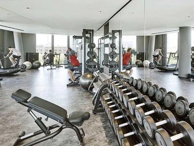 Nowoczesna siłownia z ciężarami, ławkami i dużymi oknami z widokiem.