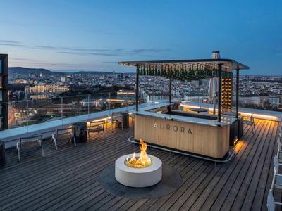 Dachterrasse mit Holzdeck, Sitzbank, Feuerschale und Sitzbereich mit Blick auf Stadt bei Dämmerung.