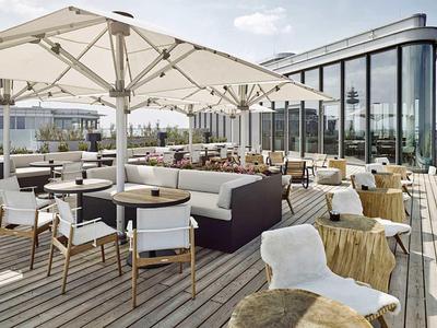 Nowoczesny taras na dachu z miejscami do siedzenia i dużymi parasolami, z widokiem na miasto.
