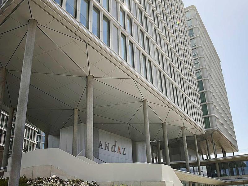 Nowoczesny wieżowiec z wieloma oknami, oświetlony światłem słonecznym i otoczony roślinami.