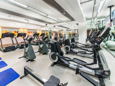 Moderní posilovna s různým kardio a tréninkovým vybavením, velkými zrcadly a jasným osvětlením.