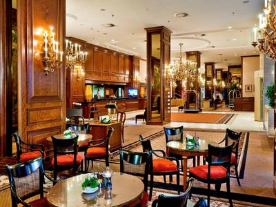 Elegantní hotelová lobby s dřevěnými stěnami, stoly, židlemi s červenými polštáři a lustry.