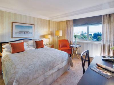 Světý hotelový pokoj s manželskou postelí, oranžovými akcenty a oknem s výhledem do zeleně.