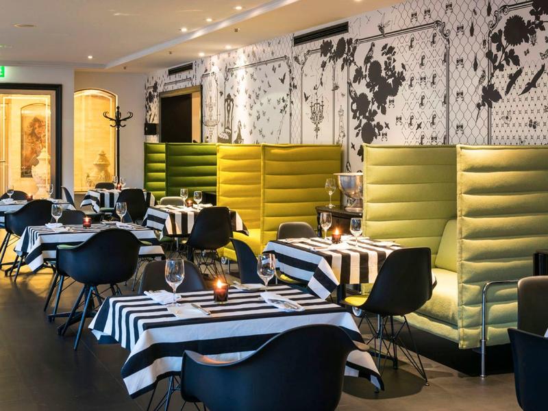 Moderní interiér restaurace s pruhovanými ubrusy, černými židlemi a žlutými čalouněnými boxy.