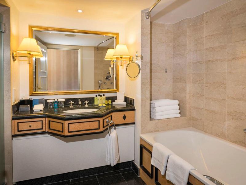 Moderní hotelová koupelna s vanou, ručníky, velkým zrcadlem a umyvadlem s lampami.