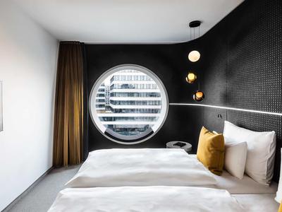 Modern hotelkamer met rond raam en gezellig tweepersoonsbed.