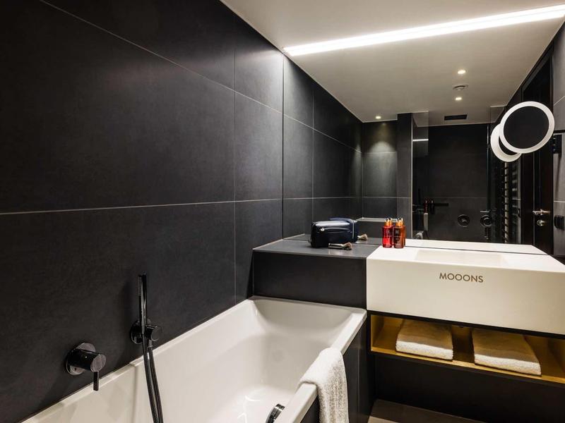 Moderne badkamer met wit bad, wandspiegel en minimalistische wastafel in donker design.