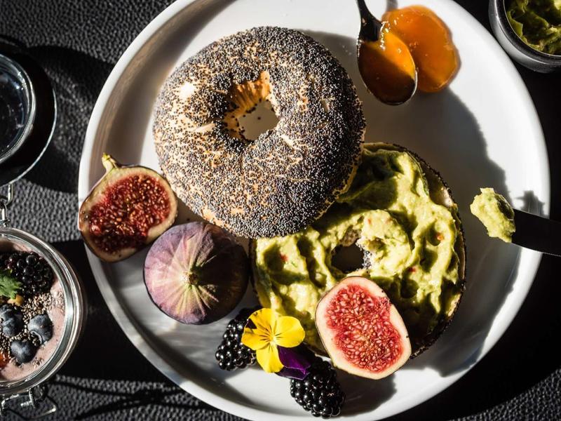 Ontbijtbord met bagel, avocadopuree, vijgen, bramen en honing.