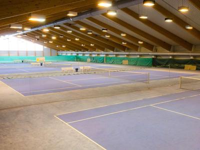 Grote indoor tenniszaal met meerdere banen onder houten plafond en goede verlichting.