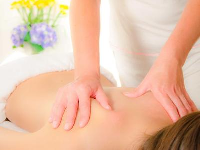 Osoba otrzymująca masaż pleców w jasnym, relaksującym otoczeniu z kwiatami.