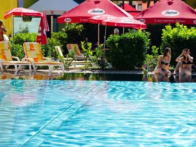 Basen z czystą niebieską wodą, leżakami i czerwonymi parasolami na zewnątrz hotelu.