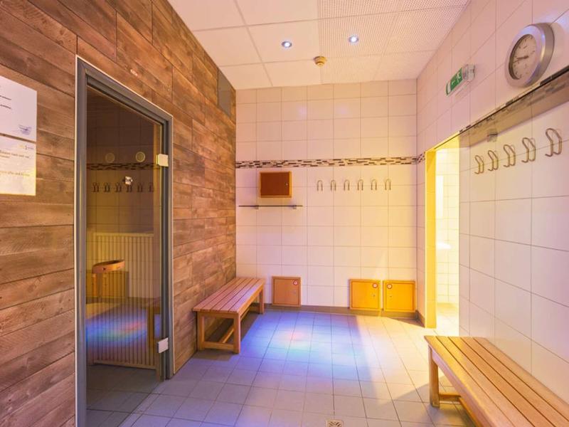 Jasno oświetlona szatnia sauny z drewnianymi ławkami i haczykami na ubrania.