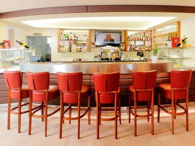 Zona de bar moderna en hotel con taburetes rojos y estanterías iluminadas al fondo.