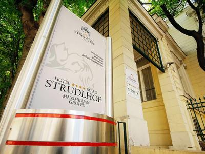 Área de entrada de un hotel con un cartel blanco y cintas rojas en una pared de piedra arenisca.