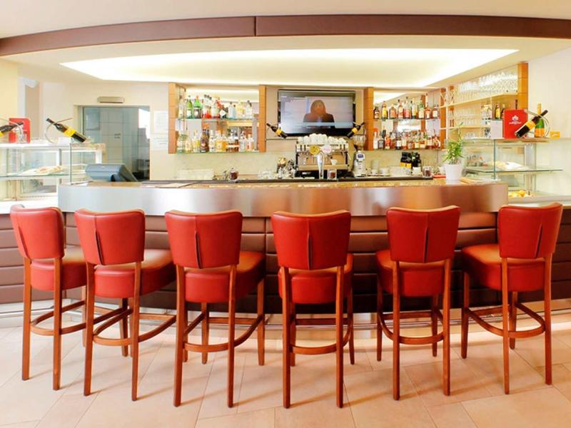 Moderner Bartresen mit sieben roten Barhockern vor Regalen voller Flaschen und Gläser.