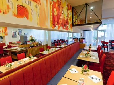 Nowoczesna restauracja z czerwonymi ławkami, jasnymi stołami i kolorową dekoracją ścian.