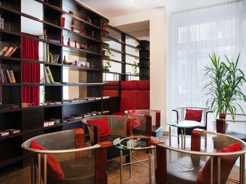 Salon moderne avec étagères foncées, coussins rouges et tables en verre.