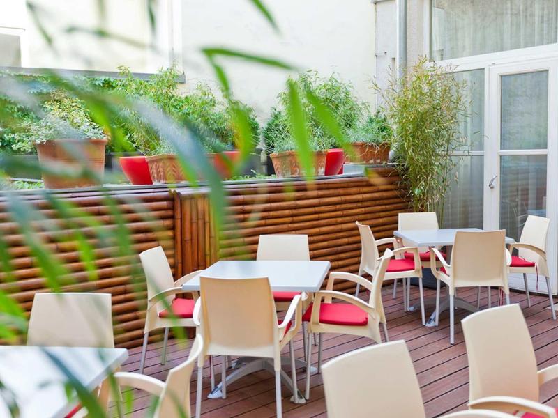 Espace extérieur de l'hôtel avec tables et chaises couvertes sur une terrasse en bois.