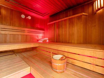 Traditionele houten sauna met banken en emmer water verlicht door warm rood licht.
