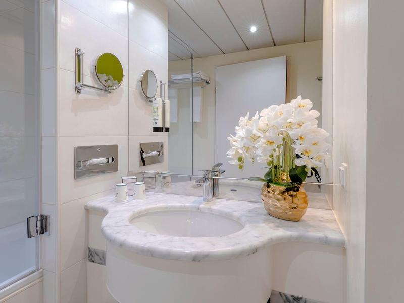 Lichte hotelbadkamer met ronde wastafel, grote spiegel en bloemenarrangement.