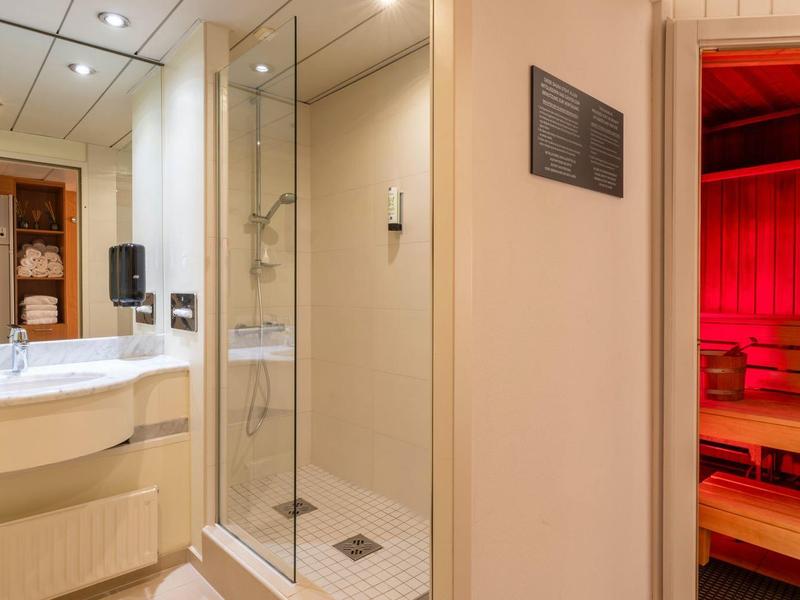 Heldere badkamer met douche, wastafel en aangrenzende sauna met rood licht.