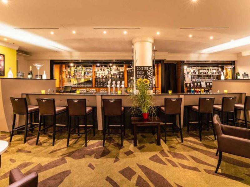 Moderne hotelbar met krukken, warme verlichting en meerkleurig tapijt.