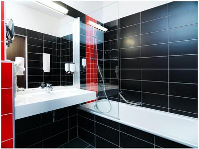 Moderní koupelna s černými obklady na stěnách, bílým umyvadlem a vanou se sprchou.