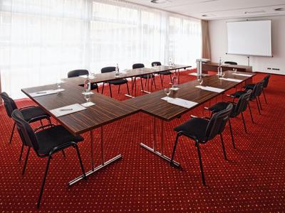 Konferenční místnost s U-tvarovaným stolem, červeným kobercem a velkými okny