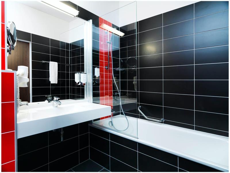 Moderní koupelna s černými dlaždicemi, bílou vanou a umyvadlem.