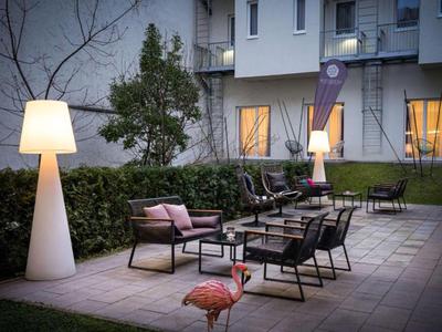 Abendliche Außensitzgruppe mit modernen Stühlen, Tischen und großen Stehlampen vor einem Hotel.