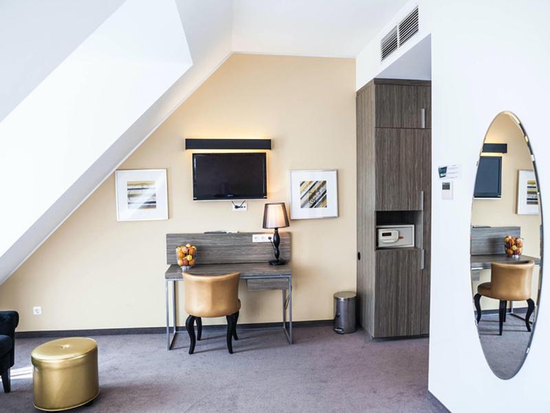 Chambre d'hôtel moderne avec plafond incliné, bureau, télévision et tabouret doré.