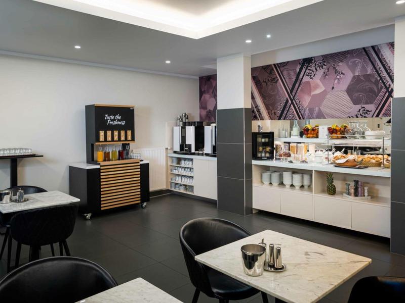 Salle de petit déjeuner moderne avec machine à café, snacks et espaces assis dans un cadre lumineux.