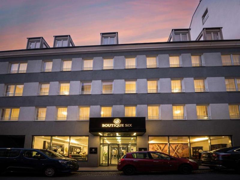 Immeuble d'hôtel à plusieurs étages au crépuscule avec fenêtres éclairées et voitures garées.