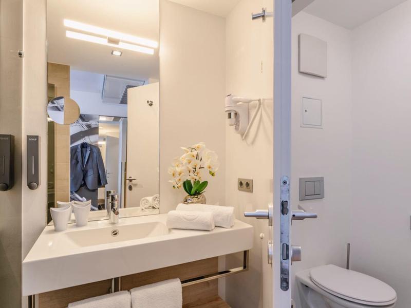 Světla koupelna s bílým umyvadlem, toaletou a velkými zrcadly.