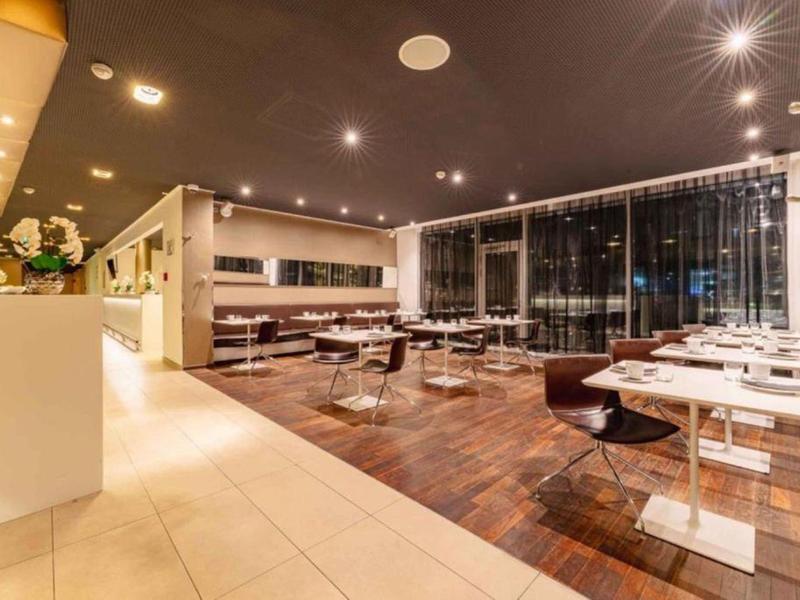 Moderní, dobře osvětlená restaurace s bílými stoly a tmavými židlemi vedle velkých oken.