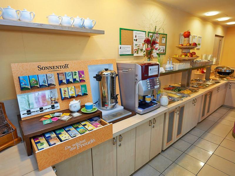 Buffetgedeelte met koffieautomaten, theeselectie en diverse ontbijtfaciliteiten in een hotelachtige ruimte.