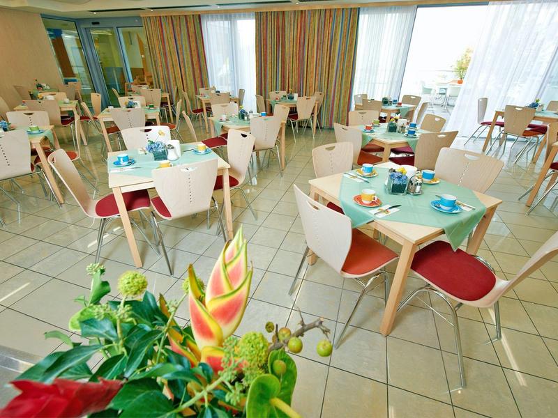 Lichte eetzaal met meerdere gedekte tafels en rode stoelen in zonovergoten kamer.