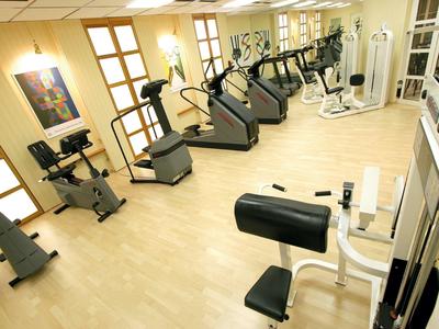 Helles Fitnessstudio mit Holzfußboden, mehreren Laufbändern, Fahrrädern und Kraftgeräten.