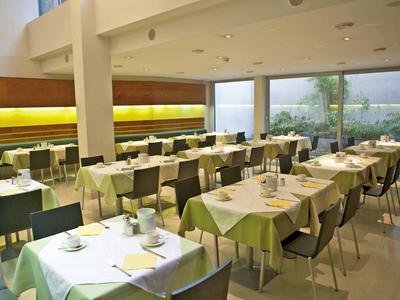 Heller, moderner Speisesaal mit Tischen, Stühlen und grünen Tischdecken in Reih und Glied.