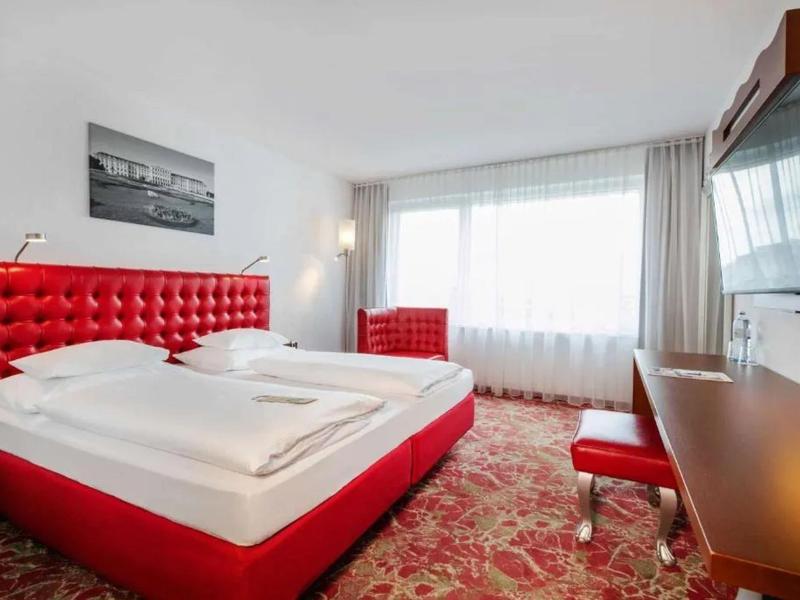 Habitación de hotel moderna con cama roja, escritorio y gran ventana con cortinas.