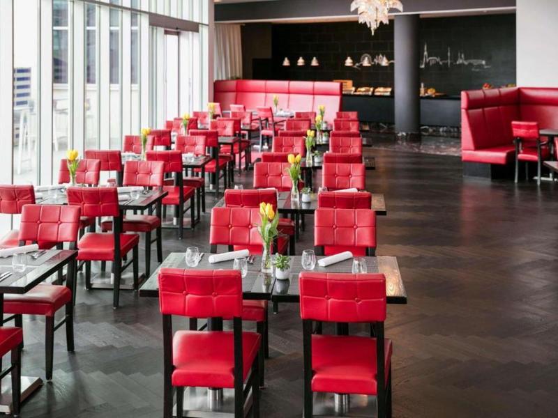 Restaurante moderno con sillas rojas y mesas junto a grandes ventanales, suelo de madera oscura.