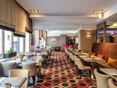 Modernes Restaurant mit vielen Tischen, bequemen Stühlen und Teppich mit buntem Kreis-Muster.