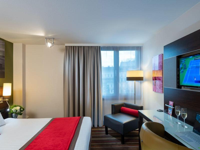 Moderne hotelkamer met groot bed, rode accenten en uitzicht uit het raam.