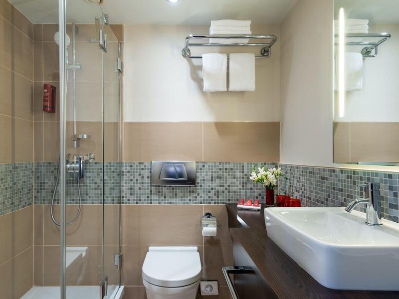 Moderne hotelbadkamer met inloopdouche, toilet, wastafel en handdoeken aan de muur.