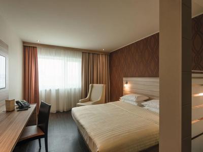 Modern hotel room with double bed, desk, and cozy armchair in natural daylight.