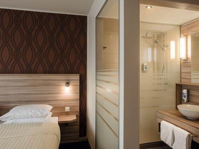 Modern hotel room with double bed next to a glass door leading to bathroom with sink and shower.